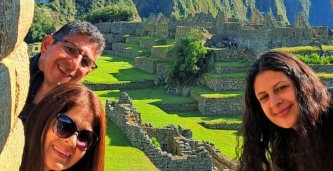 Familia de viajeros asomándose entre muros incas en la portada del tour a Machu Picchu de 1 día. Viajes en Cusco.