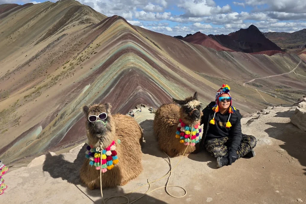 Viajera junto a dos alpacas frente a la Montaña de 7 Colores Vinicunca en los Andes de Cusco, Perú