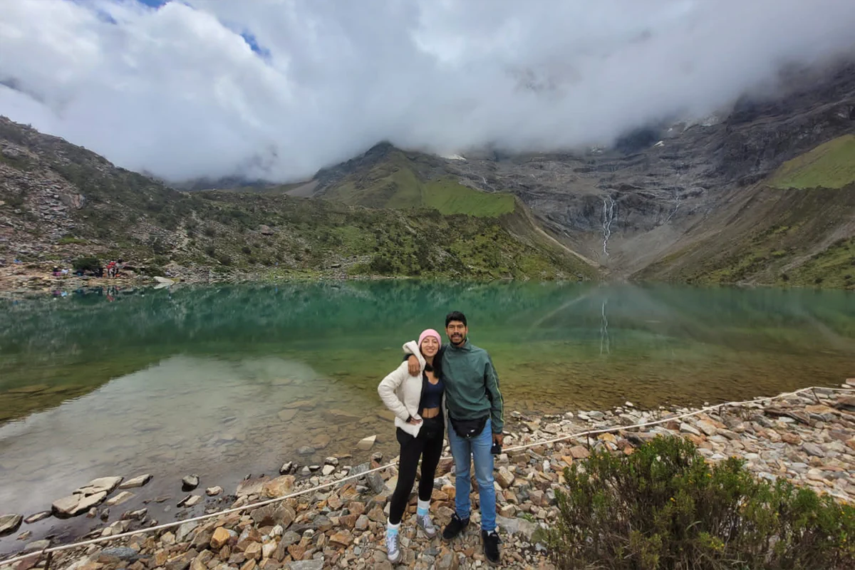 Pareja de viajeros frente a las aguas turquesas de la Laguna Humantay en la cordillera de Cusco, Perú