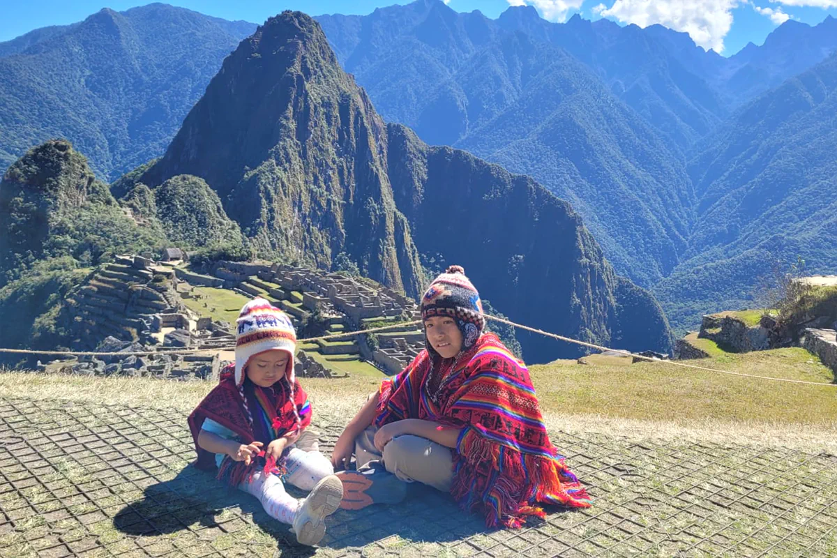 Niños felices vistiendo ponchos andinos tradicionales en el mirador de la ciudadela de Machu Picchu en Cusco
